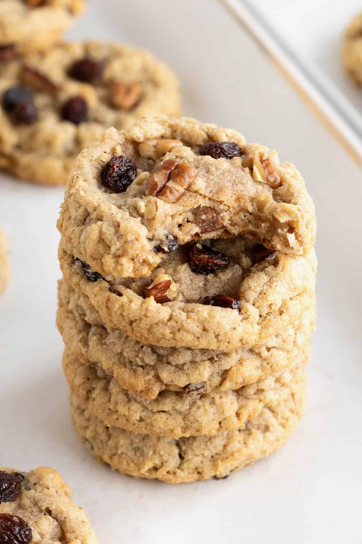 A stack of five oatmeal raisin cookies with pecans. The top cookie has a bite out of it.