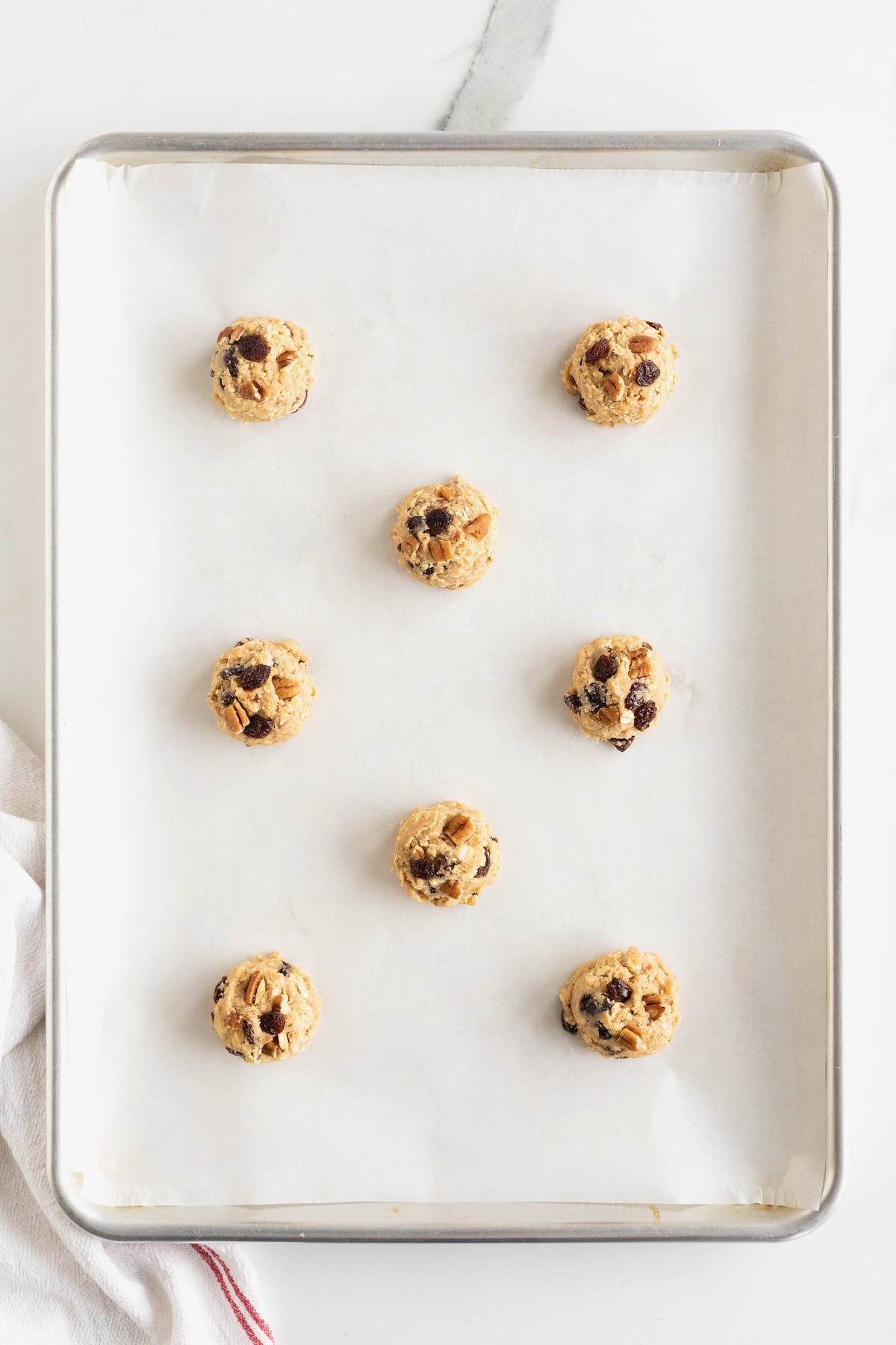 Eight oatmeal cookie dough balls on a parchment lined aluminum baking sheet.