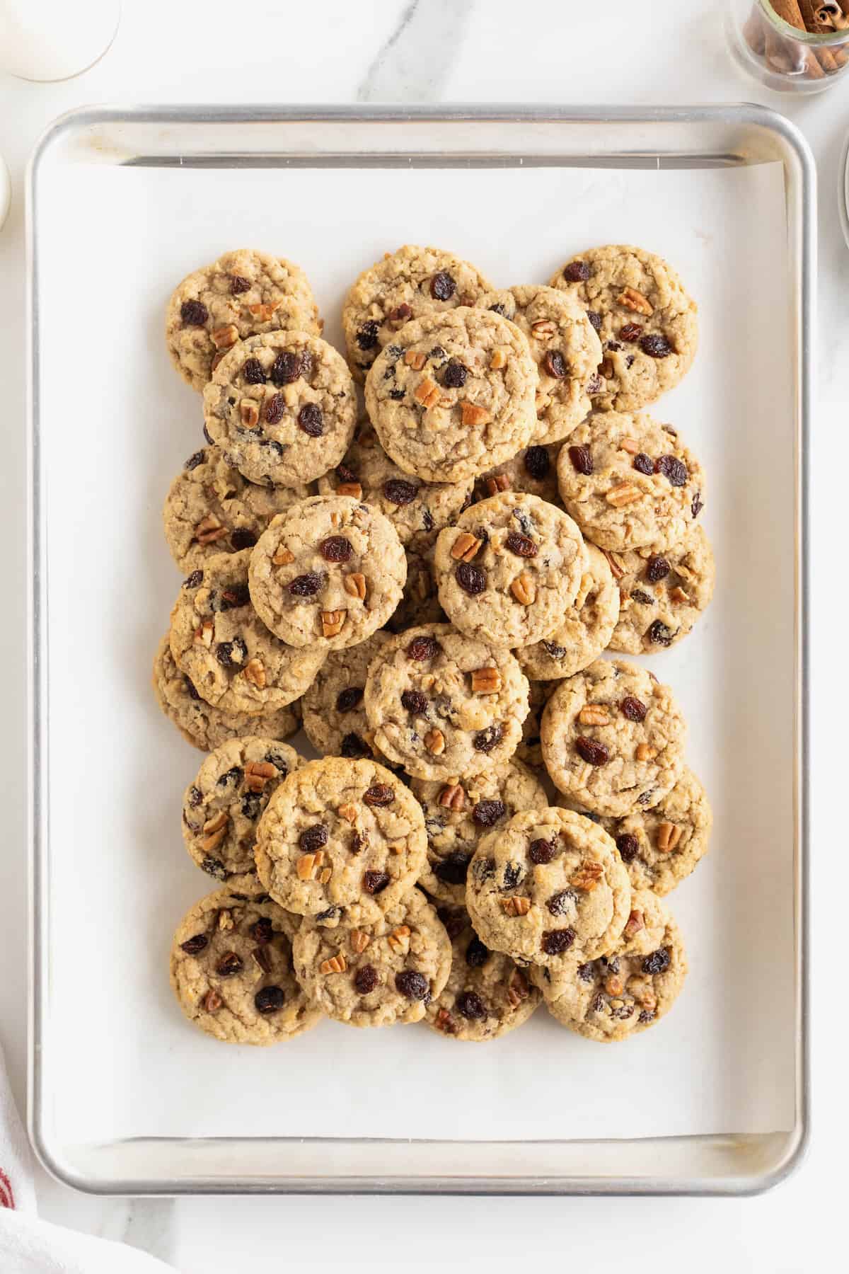 A parchment lined aluminum baking sheet piled high with oatmeal raisin cookies with pecans.