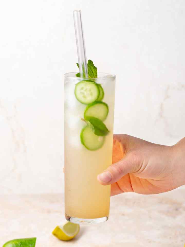 hand holding a coconut water mocktail with limes, mint and cucumber