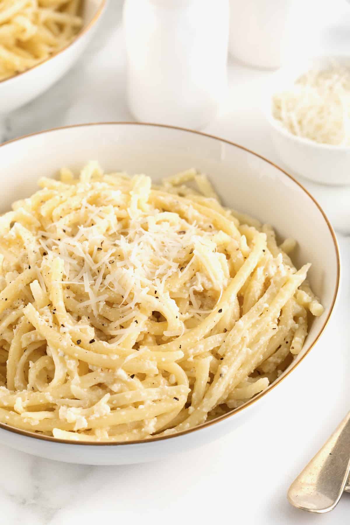 A large white, gold-rimmed serving bowl of Cacio e Pepe.