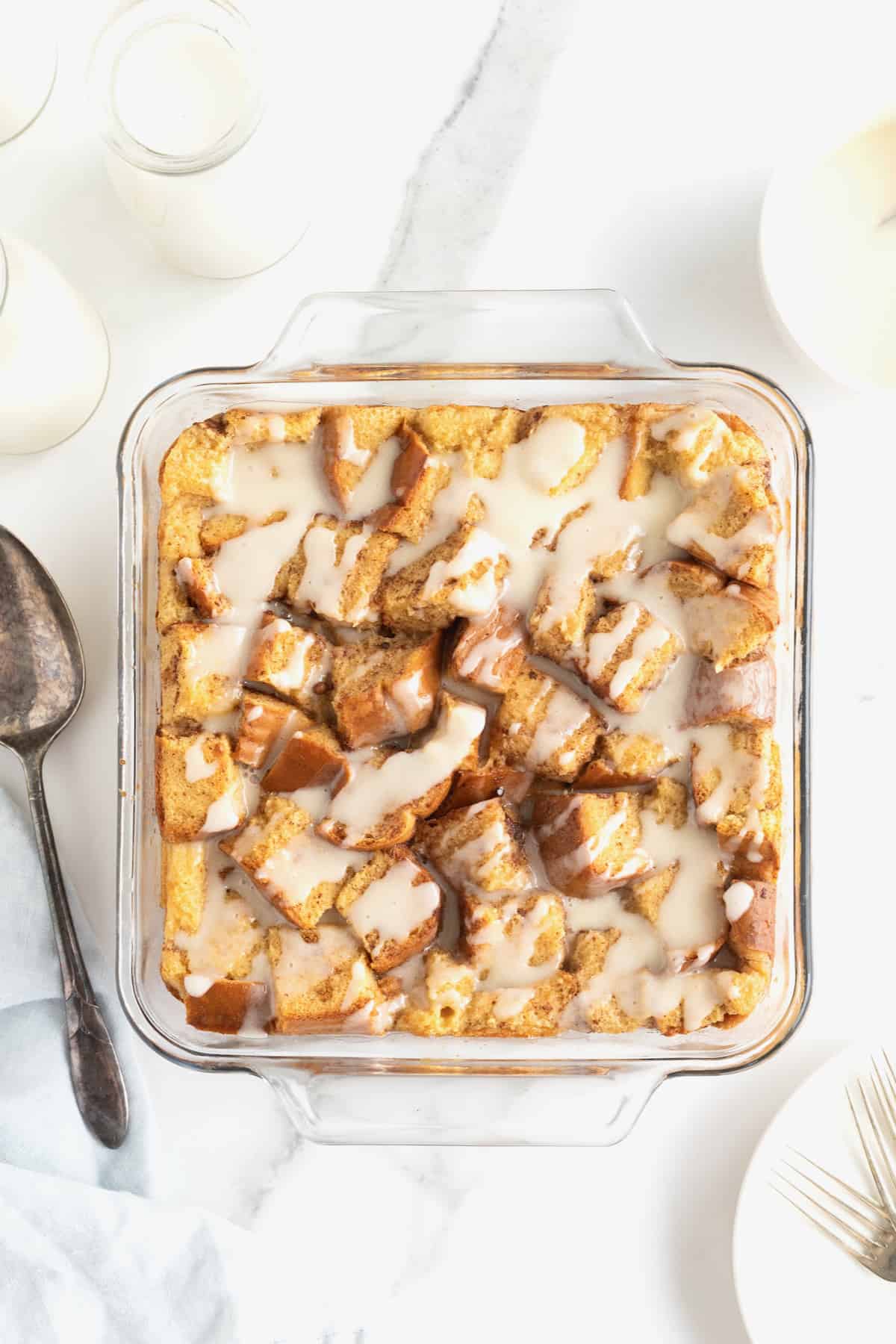 A square glass baking dish of bread pudding with white icing drizzled on top.