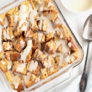 A square glass baking dish of bread pudding with white icing drizzled on top.