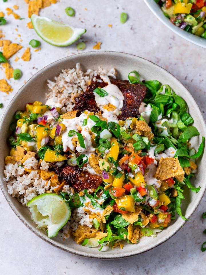 large bowl with a bed of brown rice, blackened salmon fillet, shredded lettuce, mango salsa, lime wedge and creamy chipotle sauce