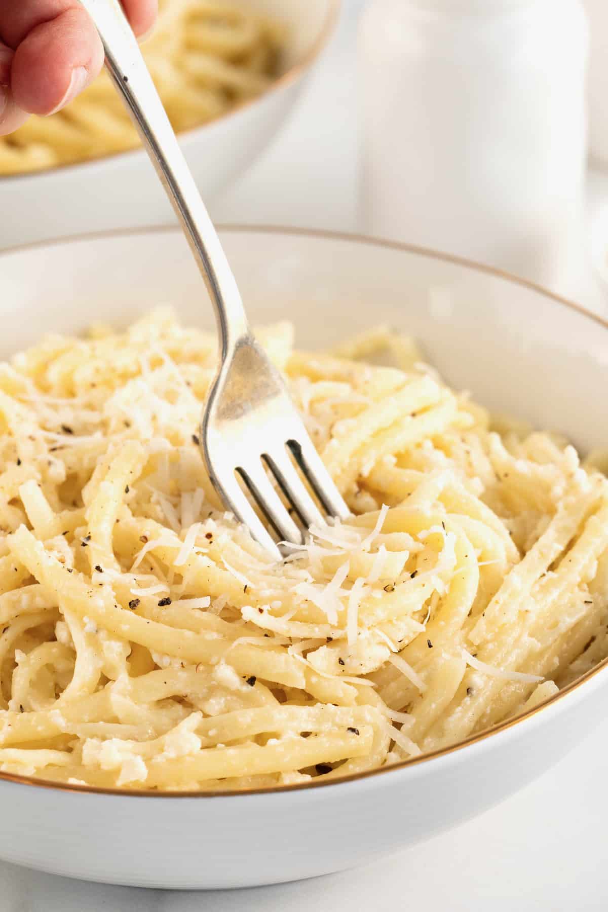 A fork in a white gold-rimmed bowl of pasta sprinkled with grated white cheese.