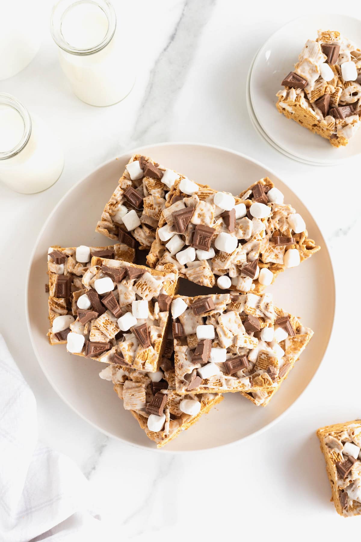 A large white plate stacked with no-bake s'mores bars on a white counter.